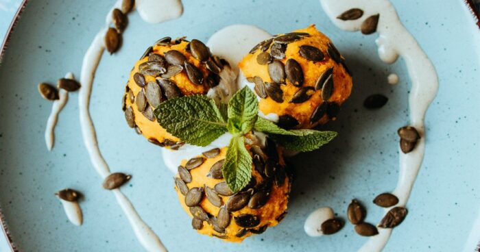 Hotové domáce slané tekvicové guľky posypte tekvicovými semienkami a maškrťte ich s jogurtom.